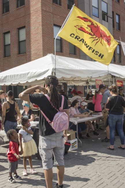 A photo of a vendor booth at the Crawfish festival. Women sitting at a plastic table under a tent are also selling raffle tickets.