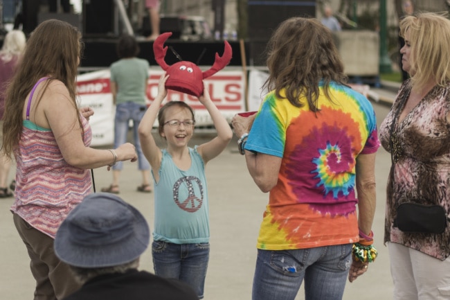 A little girl smiles, holding a red crab hat over her head. Maybe it's new?