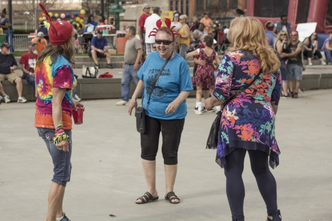 Three women dance at the crawfish festival. Two of them are wearing red hats that look like crabs for the occasion.