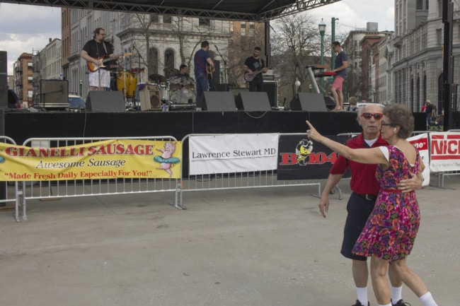 A man stands with his arm around a woman in front of the band stage. The photographer caught them mid dance.