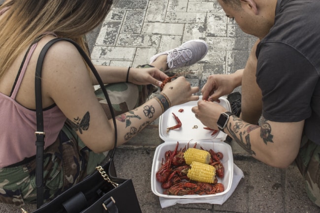 Another pair, a man and woman maybe in their 30s, share crawfish. Discarded bits of shell sit at one end of teh takeout container, while the other is filled with yet uneaten crawfish.