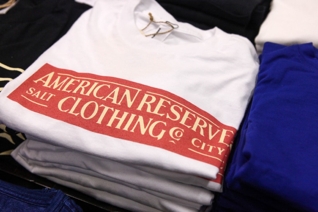 A stack of folded white shirts with a reg "American Reserve Clothing" logo across the chest.