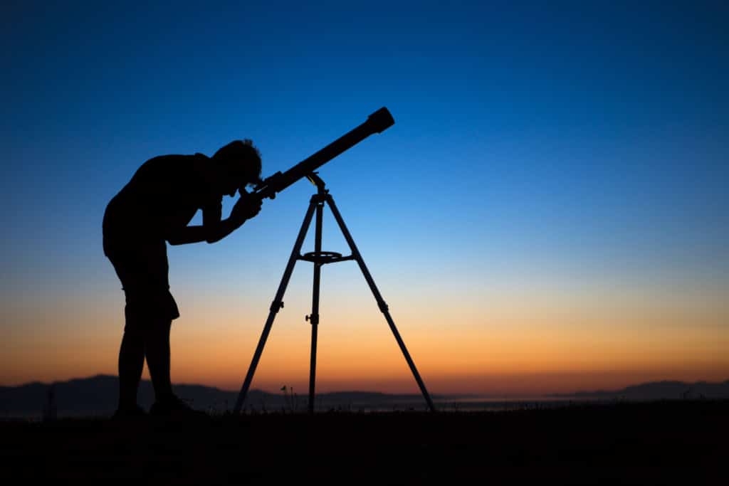 A silhouette of a boy on a clear night looking through a telescope.